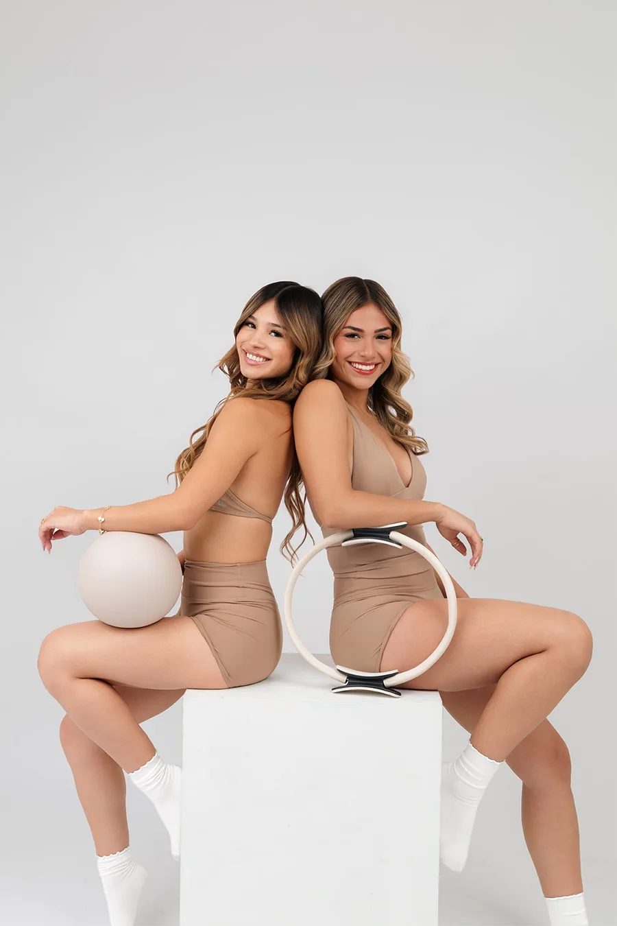 Two members sitting back to back on a studio box holding a Pilates ball and ring